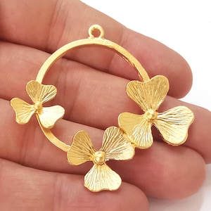 Op de afbeelding: Gouden metalen hanger met een rond frame en drie klavertjesvier-charms.