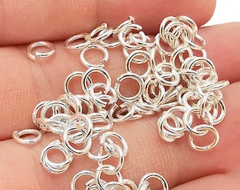 May include: A pile of silver jump rings, a type of jewelry finding, are shown on a hand. The jump rings are small and round, and they are perfect for connecting different pieces of jewelry together.