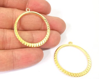 Könnte beinhalten: Zwei goldfarbene Metall-Kreis-Anhänger mit strukturiertem Design. Die Anhänger haben oben eine Öse zum Anbringen an einer Halskette oder einem Armband.