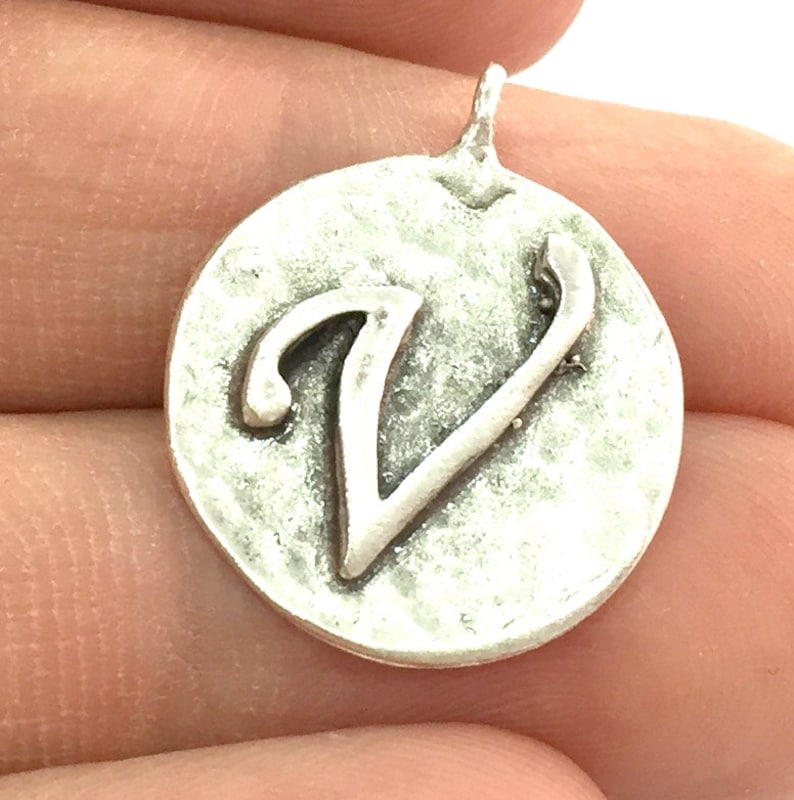 May include: Silver charm with a cursive letter V on a round disc.
