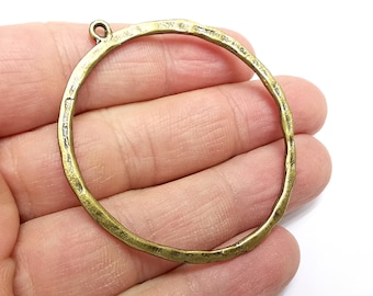 Può includere: Un grande ciondolo rotondo in metallo color oro antico con una texture martellata. Il ciondolo ha un anello nella parte superiore per attaccare una catena o un cordino.
