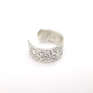 Może przedstawiać: Srebrna bransoletka typu mankiet z delikatnym, skomplikowanym wzorem kwiatowym. Bransoletka jest otwarta i ma lekko fakturowane wykończenie.