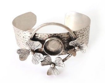 Puede incluir: Pulsera de brazalete de plata con acabado martillado y un diseño circular con tres abalorios en forma de trébol. La pulsera tiene un bisel redondo y en blanco para agregar una piedra u otro adorno.
