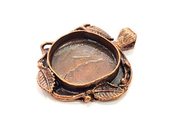 May include: A copper-toned pendant with a round, open bezel and a leafy design. The pendant has a loop at the top for attaching a chain.
