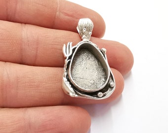 May include: Silver pendant with a large oval bezel setting. The pendant has a detailed design around the bezel and a loop at the top for attaching a chain.
