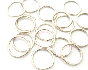May include: A pile of silver jump rings, a type of jewelry finding used for connecting chains, cords, and other jewelry components.