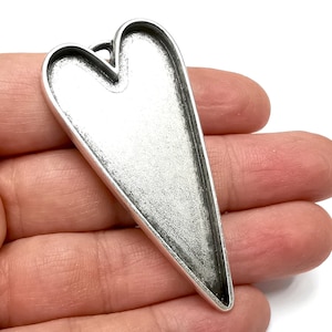 May include: A silver heart-shaped pendant with a smooth, slightly textured surface. The pendant has a loop at the top for attaching a chain or cord.