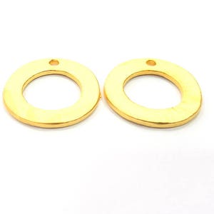 May include: Two gold-colored metal rings with a small hole at the top. The rings are smooth and have a slightly rounded edge.