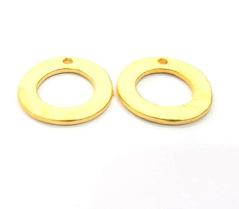 May include: Two gold-colored metal rings with a small hole at the top. The rings are smooth and have a slightly rounded edge.