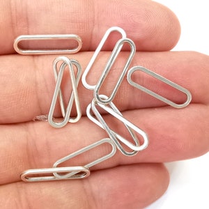 Puede incluir: Primer plano de un montón de anillos de metal ovalados plateados. Los anillos son lisos y brillantes.