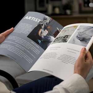 Puede incluir: Una persona est&aacute; leyendo una revista con fondo blanco y texto negro. La revista presenta el trabajo de un artista con una pintura de una persona con una camisa azul y una pintura de un dise&ntilde;o abstracto en espiral. La revista tambi&eacute;n incluye el nombre del artista y el t&iacute;tulo de la pintura.