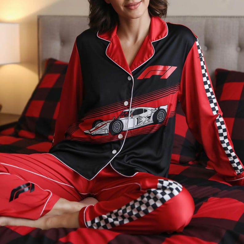 May include: Red and black pajama set with a Formula 1 race car design. The top is black with red sleeves and white trim, featuring a race car graphic. The pants are red with a checkered pattern on the cuffs. The set is made of a silky material.