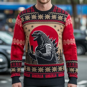Può includere: Un maglione natalizio nero, rosso e beige con Godzilla davanti a un sole rosso e uno skyline. Il maglione presenta motivi a fiocco di neve e geometrici, con la parola "GODZILLA" ripetuta in basso.