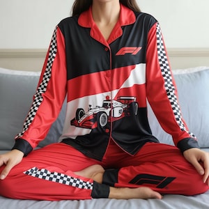 May include: Red and black pajama set with a Formula 1 racing theme. The top features a race car graphic and the F1 logo. The sleeves and pant cuffs have a checkered flag pattern.