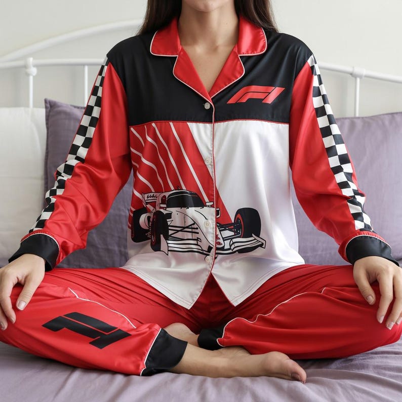 May include: Red, black, and white satin pajama set with a Formula 1 racing theme. The top features a race car graphic and the F1 logo. The sleeves have a checkered flag design. The pants are red with the F1 logo on the left leg.