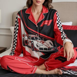 May include: Red and black satin pajama set with a race car design. The top features a button-down front, white trim, and a checkered pattern on the sleeves. The pants are red with a matching race car logo.