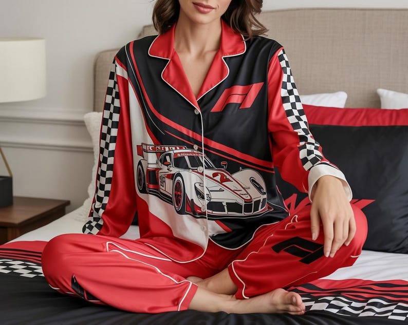 May include: Red and black satin pajama set with a race car design. The top features a button-down front, white trim, and a checkered pattern on the sleeves. The pants are red with a matching race car logo.