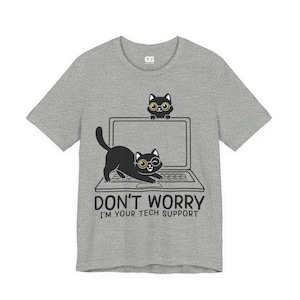 Op de afbeelding: Een grijs t-shirt met een afbeelding van twee zwarte katten met een bril en een laptop. De tekst "DON'T WORRY I'M YOUR TECH SUPPORT" staat eronder. Ronde hals en korte mouwen.