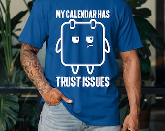 May include: Royal blue t-shirt with the white text "MY CALENDAR HAS TRUST ISSUES". The shirt features a white graphic of a calendar with a grumpy face. The person is wearing blue jeans.