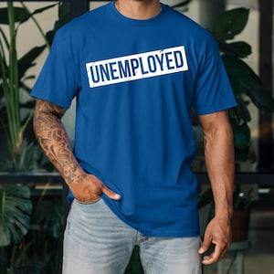 May include: A royal blue t-shirt with the word "UNEMPLOYED" printed in a white rectangular box across the chest. The shirt is a crew neck style and appears to be made of a soft material.