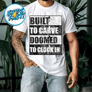 May include: White t-shirt with a black graphic design. The design features the words "BUILT TO CARVE DOOMED TO CLOCK IN" in a bold, distressed font. The shirt is a classic crew neck style.