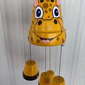 May include: A yellow and brown wind chime with a giraffe face on the top and four smaller yellow and black pots hanging below.