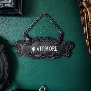 May include: A black metal sign with ornate detailing hangs from a chain. The sign reads "NEVERMORE" in white lettering.