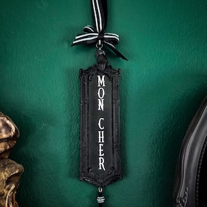 May include: Black and white ornament with a black ribbon and a black and white bead. The ornament has the words "Mon Cher" written on it.