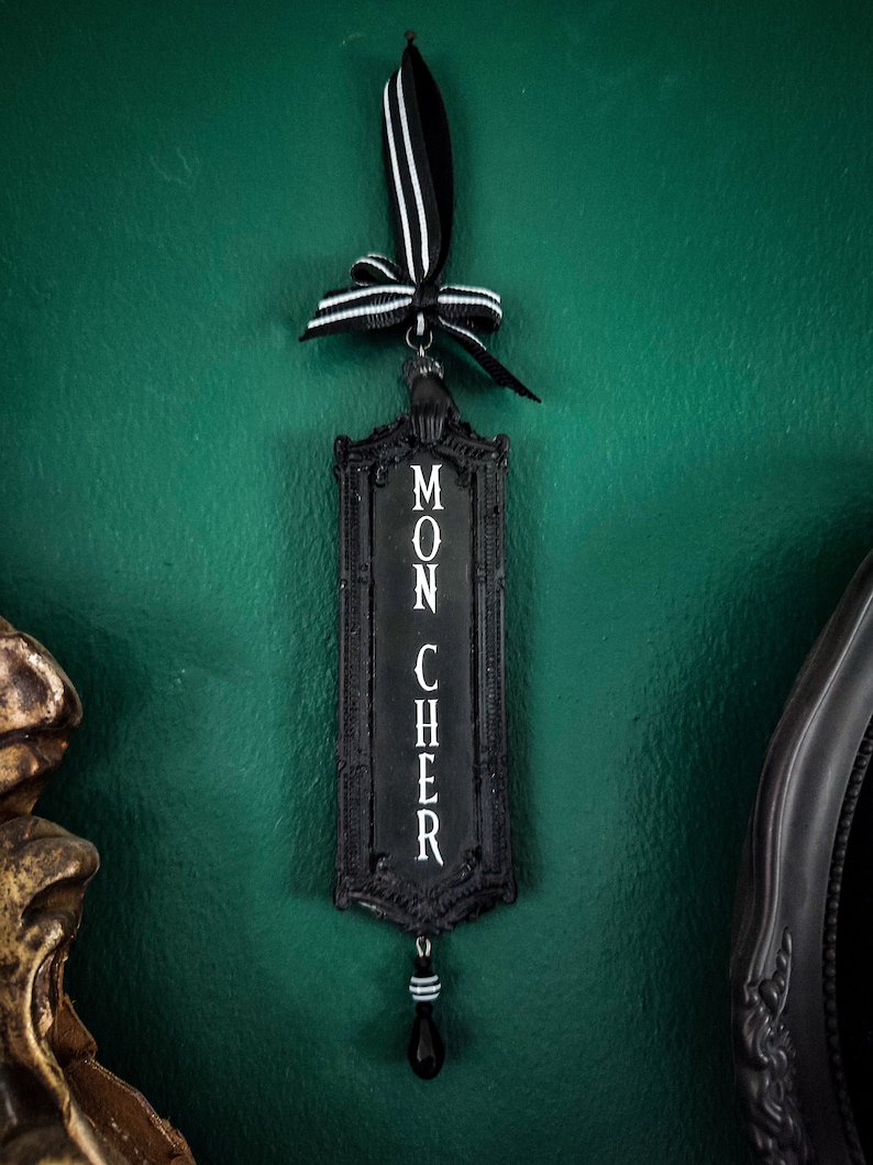 May include: Black and white ornament with a black ribbon and a black and white bead. The ornament has the words "Mon Cher" written on it.