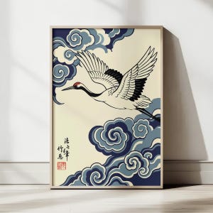 May include: Framed art print featuring a Japanese crane in flight. The crane has white feathers with black wingtips and a red head. It flies against a cream background with stylized blue clouds. The print includes Japanese text and a red seal.