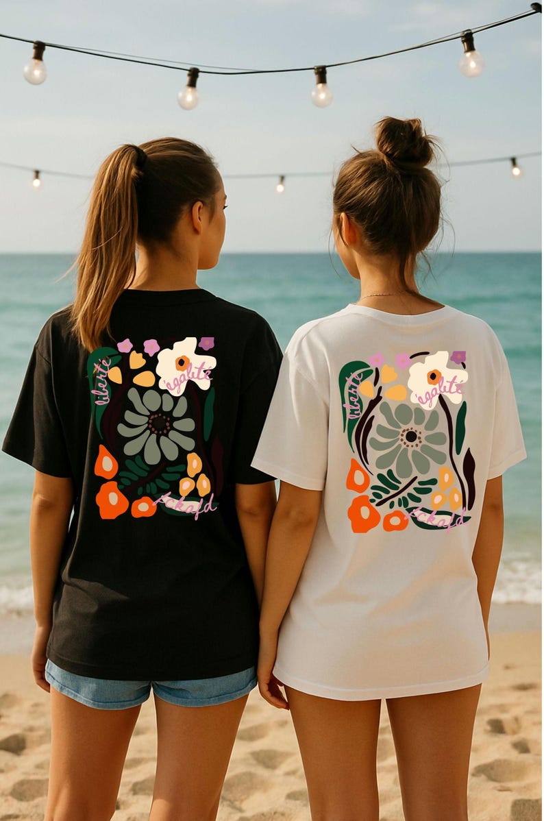 Puede incluir: Dos personas con camisetas negras y blancas con dise&ntilde;os florales. Las camisetas presentan un gr&aacute;fico rectangular con flores, hojas y texto. La camiseta negra tiene detalles en naranja y verde, mientras que la blanca tiene detalles en naranja y morado. El fondo es una escena de playa.