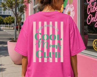 Puede incluir: Una camiseta de manga corta de color rosa brillante con un gráfico en la espalda que presenta rayas verticales de color rosa claro y el texto verde "PROUD MEMBER OF THE COOL MOMS CLUB Est 2022" en letras negritas y cursivas.