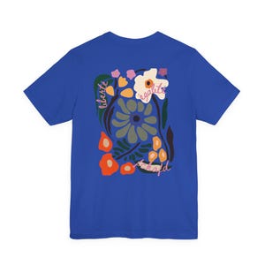 Puede incluir: Camiseta azul real con un dise&ntilde;o floral y las palabras "libert&eacute;", "&eacute;galit&eacute;" y "fraternit&eacute;". El dise&ntilde;o incorpora elementos florales naranjas, blancos y verdes. La camiseta es de cuello redondo y manga corta.