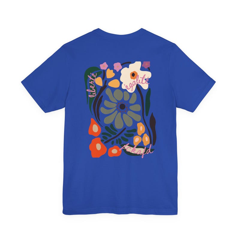 Puede incluir: Camiseta azul real con un dise&ntilde;o floral y las palabras "libert&eacute;", "&eacute;galit&eacute;" y "fraternit&eacute;". El dise&ntilde;o incorpora elementos florales naranjas, blancos y verdes. La camiseta es de cuello redondo y manga corta.