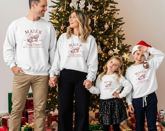 May include: Matching white crewneck sweatshirts featuring a red graphic of a vintage truck carrying a Christmas tree, with the text MAIER, EST 2020, Family Christmas, and BERLIN WINTER WONDERLAND printed in red on the chest of each garment.