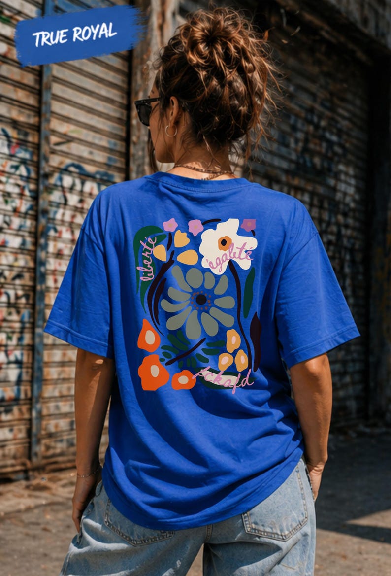 Puede incluir: Una camiseta azul real con un dise&ntilde;o floral en la espalda, con las palabras "libert&eacute;", "&eacute;galit&eacute;" y "fraternit&eacute;". La camiseta tiene mangas cortas y cuello redondo. El texto "TRUE ROYAL" est&aacute; en una pancarta azul en la parte superior.