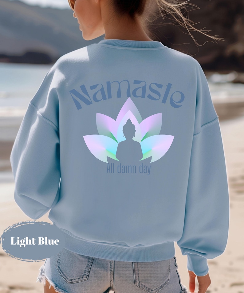 May include: Light blue sweatshirt with the word "Namaste" above a lotus flower and Buddha silhouette. The text "All damn day" is below the Buddha. The sweatshirt is light blue.
