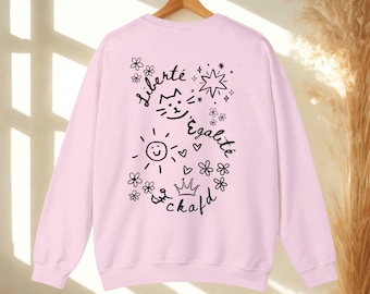 May include: A light pink sweatshirt with a crew neck. The back of the sweatshirt features black line art with the words "Liberté, Égalité, & kafd" along with a sun, cat face, star, flowers, hearts, and a crown.
