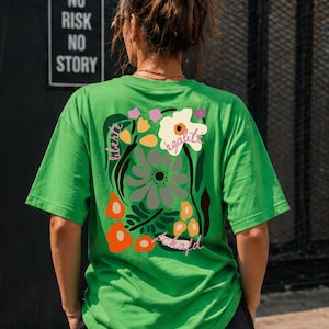 Puede incluir: Camiseta verde Kelly con un dise&ntilde;o floral en la espalda, con las palabras "liberte" y "egalite". La camiseta tambi&eacute;n tiene las palabras "fckafd" en una fuente de escritura. Las palabras "Kelly Green" est&aacute;n en una pancarta verde en la parte superior.