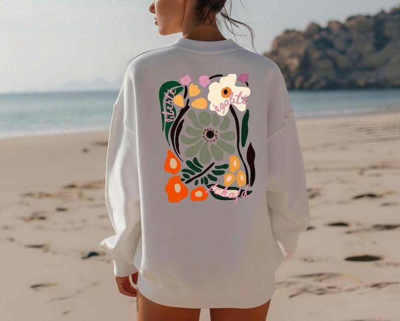 May include: White sweatshirt with a colorful floral design on the back. The design includes orange, green, pink, and white flowers with the word "egalite" in pink. The sweatshirt is a casual style, perfect for everyday wear.