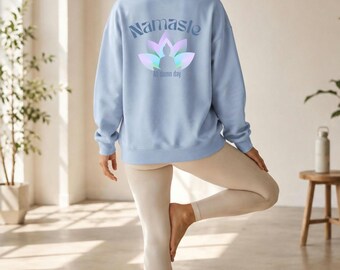May include: A light blue crewneck sweatshirt featuring a graphic on the back with the text Namaste and All damn day, centered above and below a stylized lotus flower icon with a silhouette of a person in a seated meditation pose.