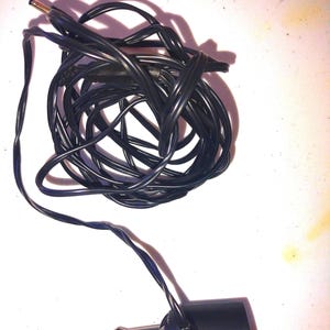 Peut inclure: Un chargeur de voiture noir avec un câble enroulé et un connecteur d'alimentation CC. Le chargeur a un corps cylindrique et un contact métallique de couleur argent. Le câble est noir et semble être fait d'un matériau flexible.