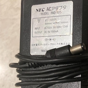 May include: Black NEC AC adapter, model PAD-105, with a label displaying technical specifications. The adapter has a black cable and a silver-colored plug. The text on the label includes "INPUT AC100V 50/60Hz 12VA" and "OUTPUT DC 9V 650mA."