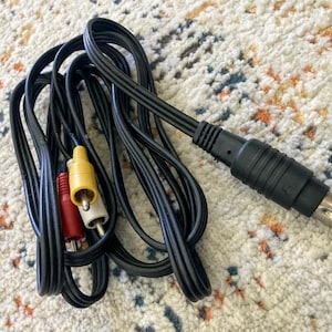 May include: Black AV cable with a multi-pin connector and three RCA connectors in red, yellow, and white. The cable is coiled on a patterned rug.