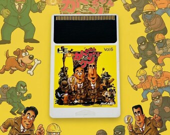 May include: A white HuCard video game cartridge for the PC Engine system, featuring a yellow label with a cartoon illustration of two men in trench coats, a dog, and various characters, labeled Vol.6 and Kato-chan Ken-chan in Japanese text.