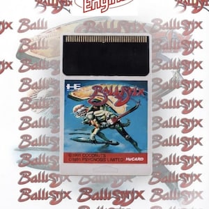 Może przedstawiać: Biała, prostokątna kaseta z grą wideo PC Engine HuCard do gry Ballistix. Etykieta posiada niebieskie tło z centralną ilustracją stworzenia trzymającego czerwoną gitarę oraz napisem Ballistix, 1991 Coconuts i 1991 Psygnosis Limited.