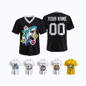 Puede incluir: Camiseta negra con cuello en V con un diseño de tiburón de dibujos animados colorido, rayos y un corazón. La parte trasera muestra "YOUR NAME" y el número "00". También se muestran camisetas blancas y amarillas adicionales con varios gráficos.