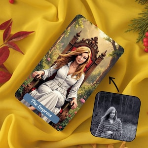 May include: A tarot card depicting a woman in a white dress seated on a throne, labelled "The Empress". A smaller black and white image of the woman is in the lower right corner. The card is set against a yellow fabric background.
