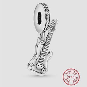 May include: A silver charm featuring a guitar pendant with a dangling loop. The guitar has detailed strings and a body shape. The loop is encrusted with small, clear stones. The word "PANDORA" is visible on the guitar.