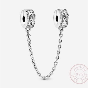 May include: A pair of silver Pandora safety chain charms. Each charm has the word "PANDORA" engraved, with a row of small clear stones. A delicate chain connects the two charms.